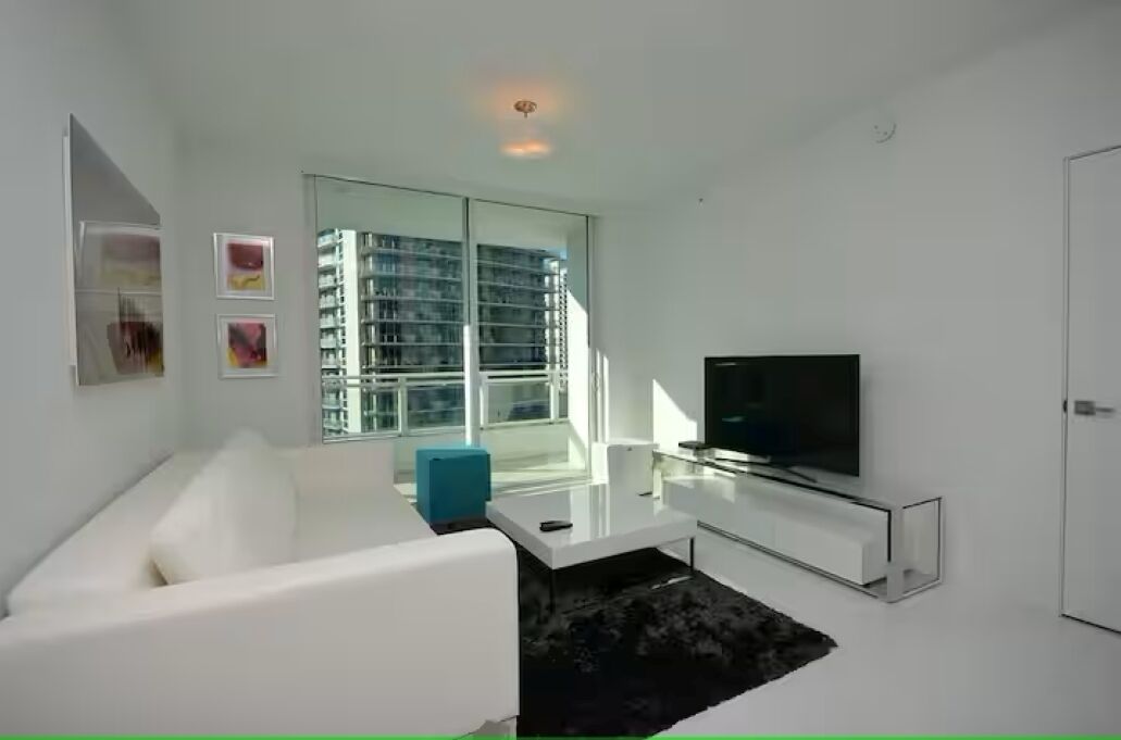Una sala de estar moderna con un sofá blanco, una mesa de centro de vidrio, un televisor de pantalla plana y una estantería.