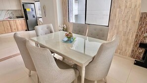 A dining area with a glass table, six chairs, and a kitchen in the background. - Vilma Luxury Rentals marina del rey laguito building (Cartagena de Indias)