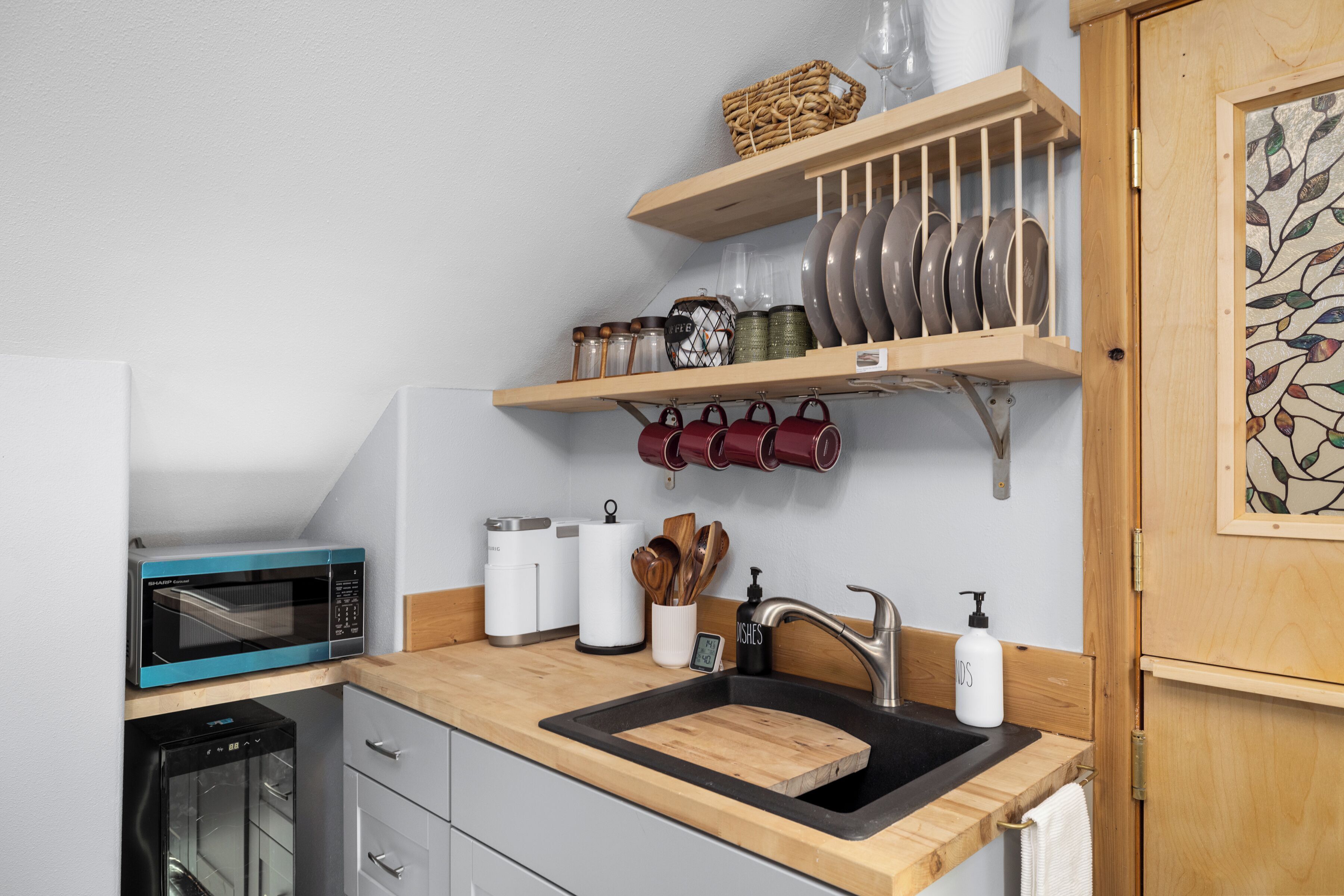 A kitchen with a microwave, oven, sink, and shelves with dishes and jars.