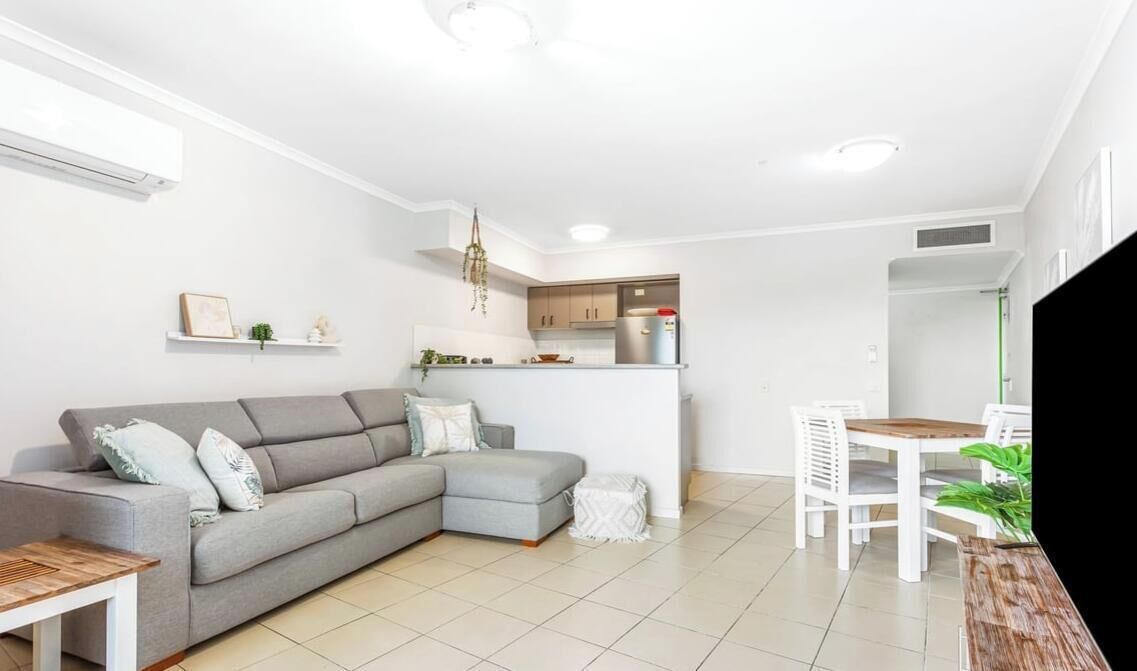 A modern living room with a grey sectional sofa, a small dining table, and a kitchen area in the background.