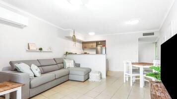 A modern living room with a grey sectional sofa, a small dining table, and a kitchen area in the background.