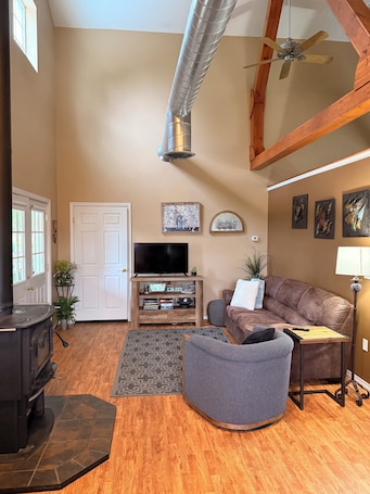 A living room with a fireplace, a sofa, a television, and a ceiling fan.. 1-bedroom cottage on a mini farm, handicap friendly in North Spokane!
