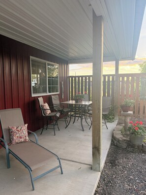A covered patio with a table and chairs, a window, and a wooden fence.