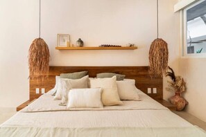 Ein Schlafzimmer mit hölzernem Kopfteil, einem Bett mit vielen Kissen, einem Regal mit Dekoration und einer Pendelleuchte.