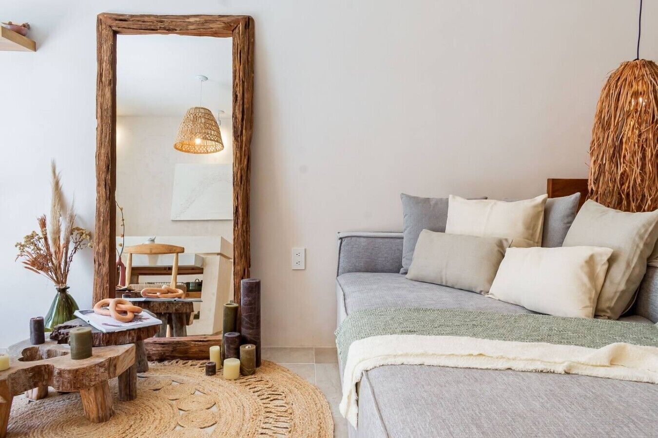 A bedroom with a large mirror, a bed with multiple pillows, a woven rug, and a rustic wooden table with candles.