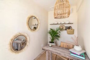 Ein Zimmer mit drei Wandspiegeln, einer Korbschichtlichtleuchte, einer Topfpflanze, einem Holztisch und einem Regal mit Dekorationsobjekten.
