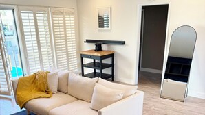 Un salon moderne comprenant un canapé, un fauteuil, une petite table, un miroir et une fenêtre avec des stores.