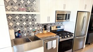 Une cuisine moderne dotée d’appareils électroménagers en acier inoxydable, d’un plan de travail en bois et d’un revêtement mural décoratif.