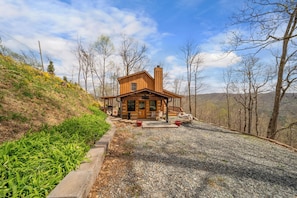 Eine Hütte mit Veranda, Schornstein und gepflasterter Auffahrt.
