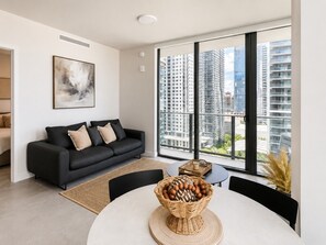 Ein modernes Wohnzimmer mit einer schwarzen Couch, einem Esstisch mit einer Korb voller Eier und einem großen Fenster mit Blick auf die Stadt.