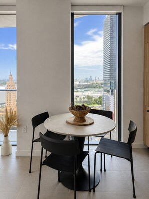 Ein moderner Essbereich mit einem runden Tisch, schwarzen Stühlen und Blick auf eine Skyline durch große Fenster.