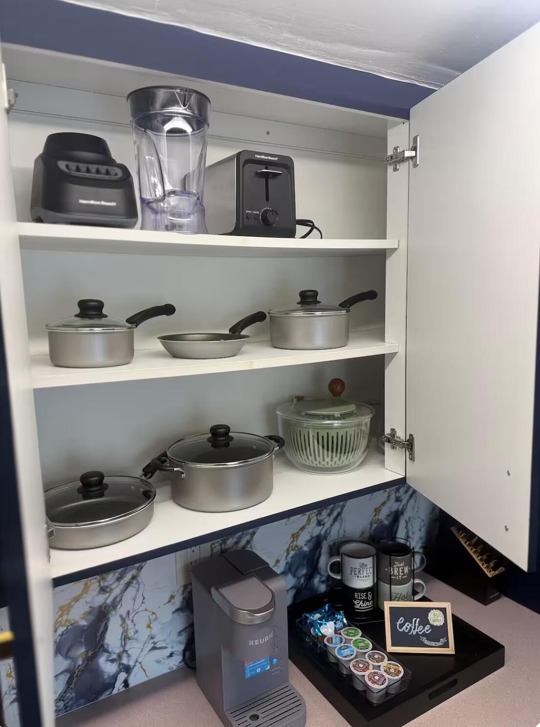 A kitchen with a coffee maker, a blender, and various pots and pans on shelves.