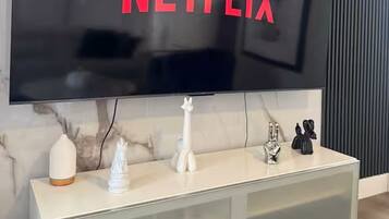 Ein modernes Wohnzimmer mit einem großen Flachbildfernseher an einer Marmorwand, einem weißen Konsolentisch mit Dekoration und einer dunkelgrauen Akustikplatte rechts.