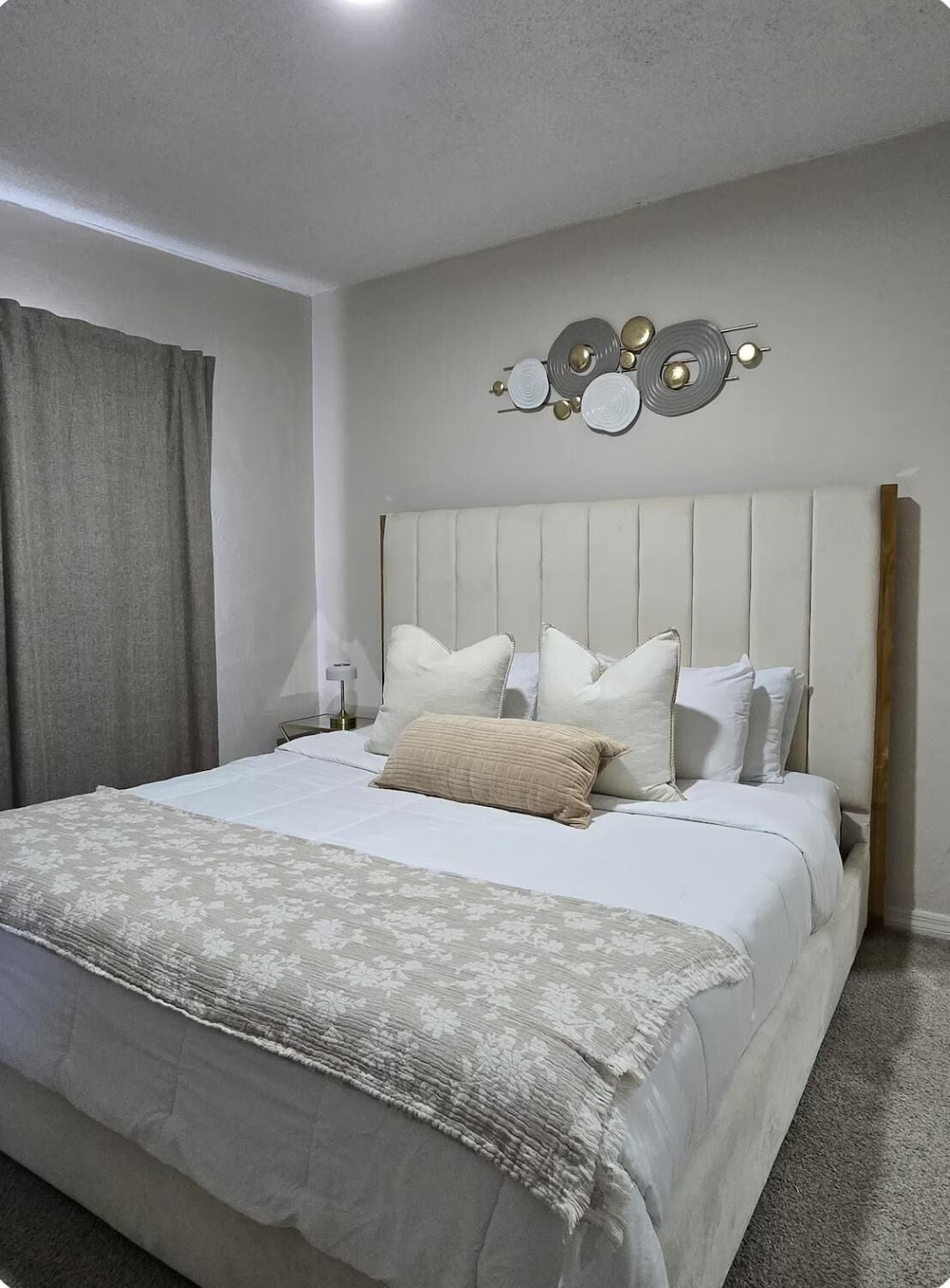 Una camera da letto con un letto, cuscini, una testiera, una decorazione a parete e una tenda.
