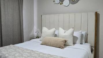 Una camera da letto con un letto, cuscini, una testiera, una decorazione a parete e una tenda.