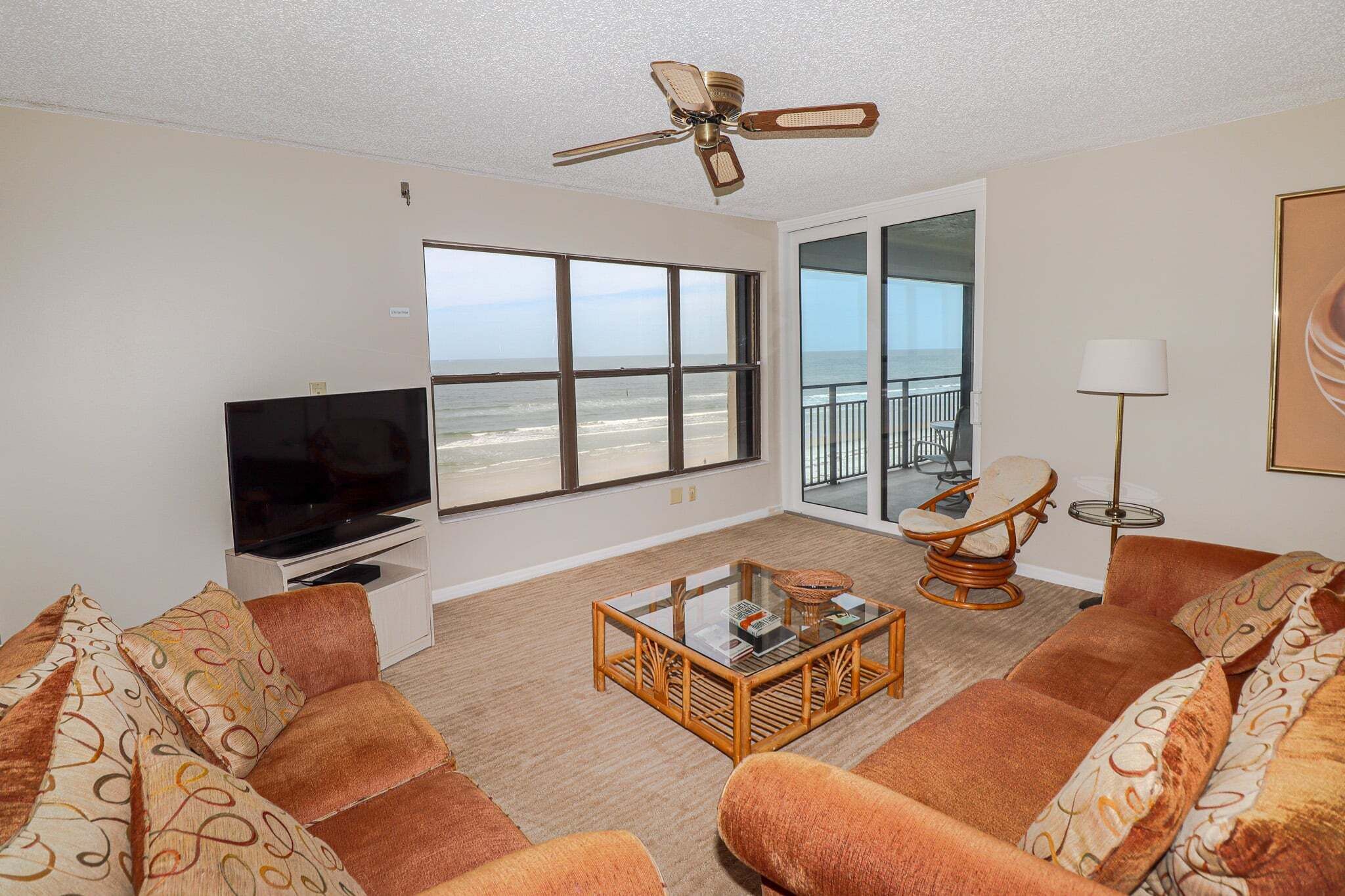Ein Wohnzimmer mit Fernseher, einem Glastisch und Blick auf den Strand.