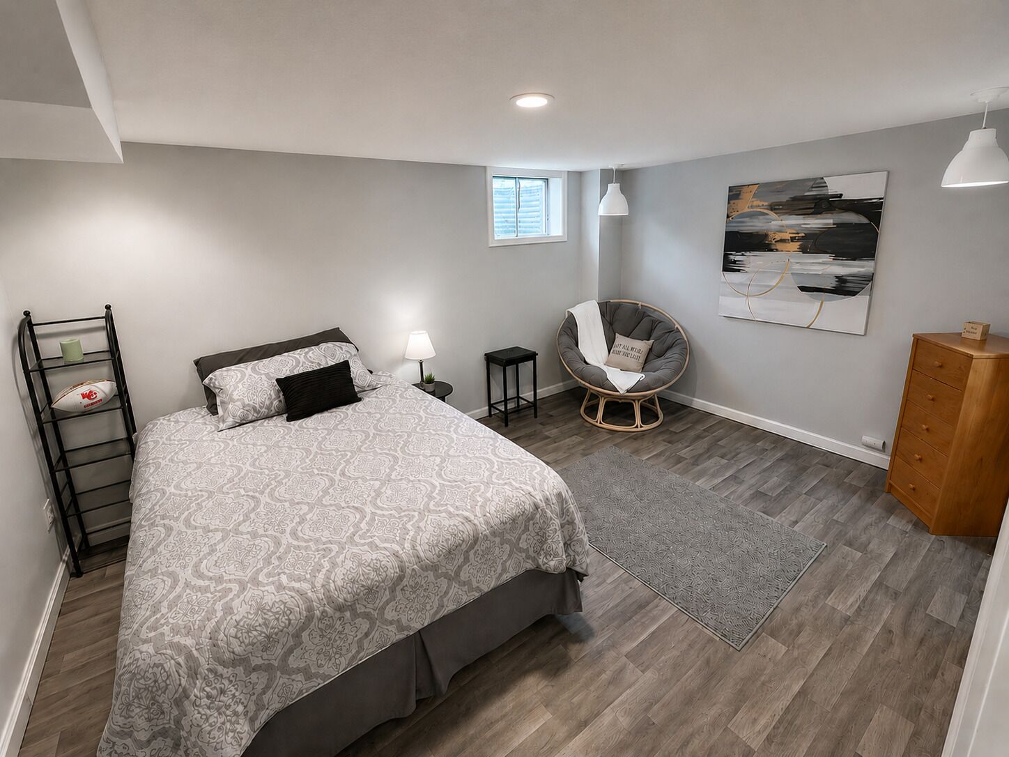 A bedroom with a bed, a chair, a dresser, a lamp, and a painting on the wall.