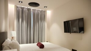 Una camera d'albergo con un letto, una televisione a muro, una finestra con tende e una lampada su un comodino.