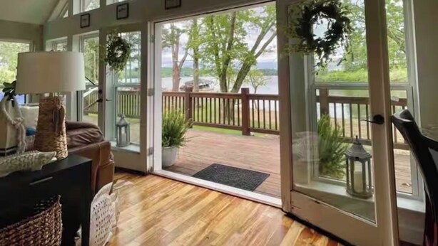 Ein geräumiges Zimmer mit großen Fenstern, einer Holterrasse und Blick auf Bäume und Wasser.