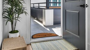 Una entrada moderna con una puerta gris, una planta en maceta, una cesta de mimbre y una alfombra texturizada.