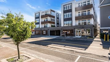 Un edificio residencial de varios pisos con balcones, un estacionamiento y un árbol pequeño en primer plano.