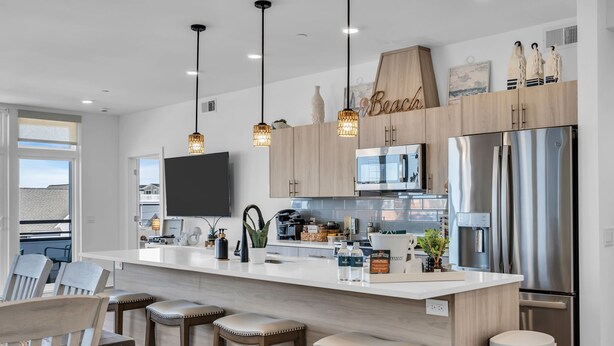 Una cocina moderna con una isla grande, electrodomésticos de acero inoxidable, iluminación colgante y vistas al exterior.