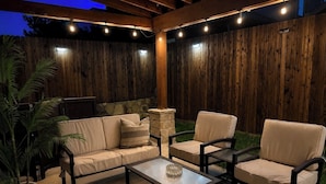 An outdoor patio with a wooden fence, a stone fireplace, and a seating area with a sofa and two chairs. - Updated, Spacious TWHM - Close to Everything - Sleeps 8 - 5min to DFW airport (Irving)