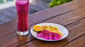 A glass of pink smoothie, a plate with dragon fruit and banana slices, and a spoon on a wooden table. - Villa Olala Penida (Penida Island)