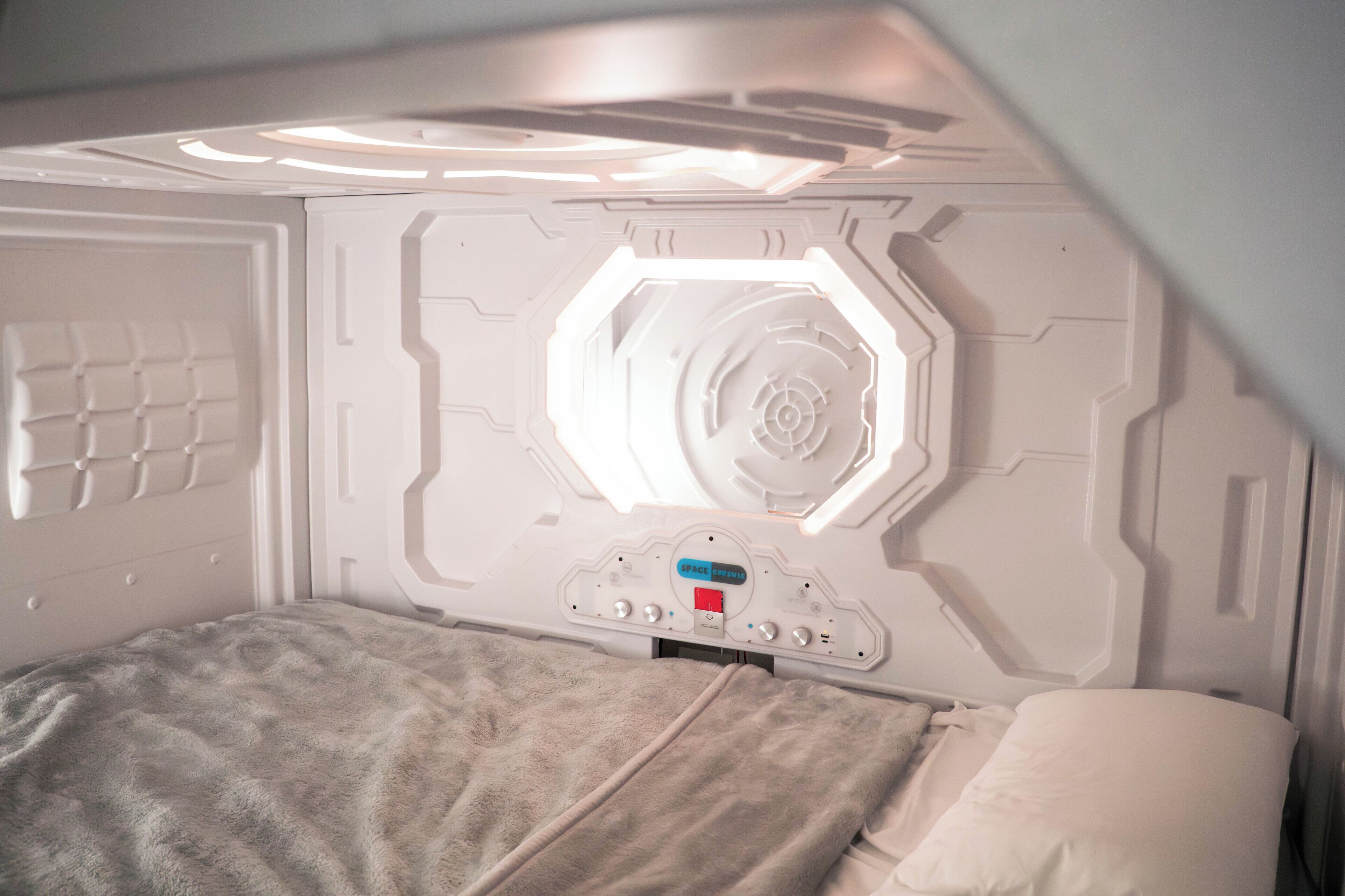 A room with a bunk bed, a control panel with a red button, and a circular light fixture on the wall.