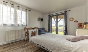 Ein Schlafzimmer mit Bett, Schreibtisch, Stuhl, Heizkörper, Fernseher und Blick ins Freie.