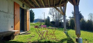 A covered outdoor area with a wooden bench, a folding table, and chairs. - Ô coeur des Volcans - MUROL (MUROL)