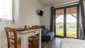 Ett rum med en säng, ett bord med stolar, en soffa, en tv som är monterad på väggen och ett stort fönster med gardiner.