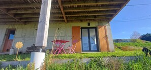 A rustic building with a wooden roof, a glass door, and a small outdoor seating area with pink chairs. - Ô coeur des Volcans - MUROL (MUROL)