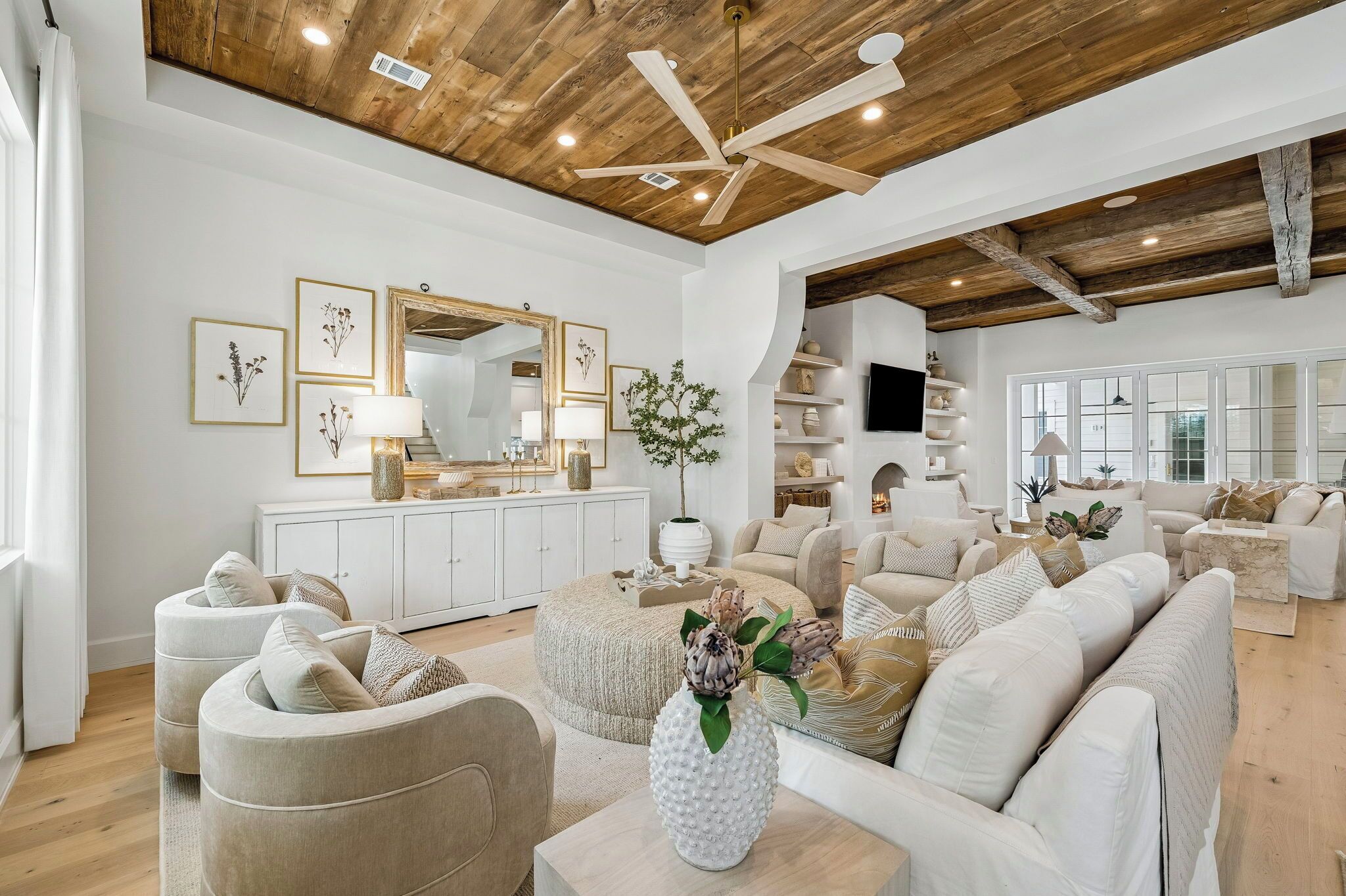 Un salon spacieux avec un plafond haut, des poutres apparentes, un ventilateur de plafond et une grande fenêtre.