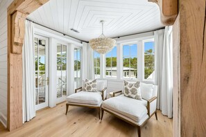 Ein Zimmer mit zwei weißen Sitzgelegenheiten, einer Pendelleuchte und großen Fenstern mit Vorhängen.