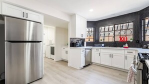 Une cuisine moderne dotée d’appareils électroménagers en acier inoxydable, de meubles blancs et d’un dosseret en carreaux noirs.