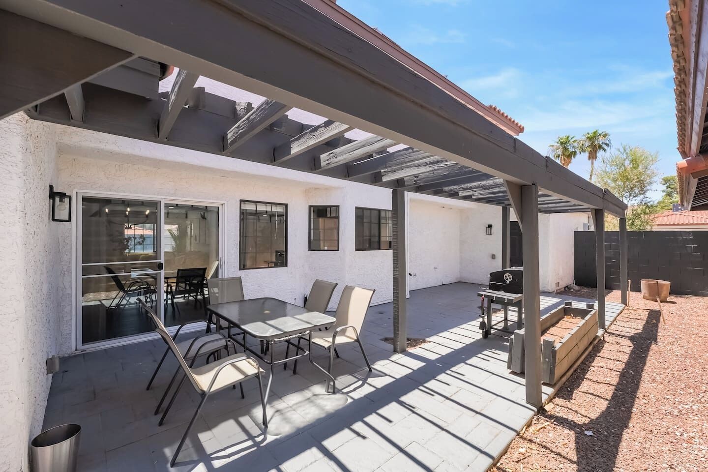 An outdoor patio with a table and chairs, a grill, and a pergola structure.