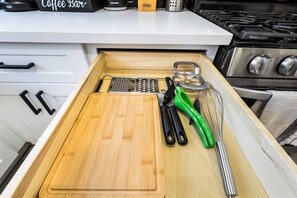 Eine Küchenschublade mit Schneidebrett, Reibe, Küchenwerkzeug mit grünem Griff und einem Metallschneebesen.