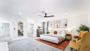 Une chambre à coucher moderne avec un grand lit, un ventilateur de plafond et des œuvres d’art accrochées aux murs.