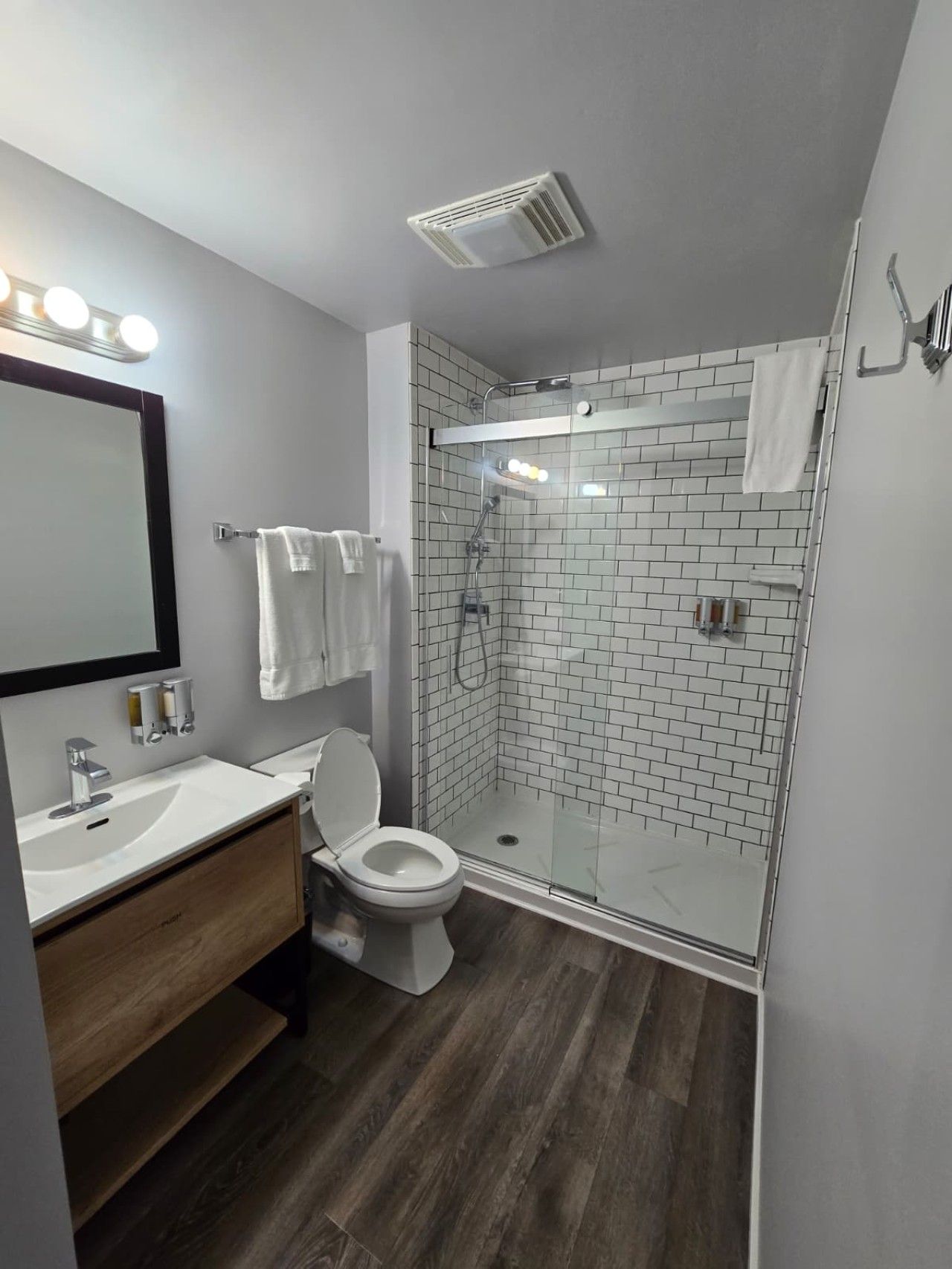 Ein modernes Badezimmer mit einer gläsernen Dusche, einer weißen Toilette, einem Waschtisch mit Spiegel und einer Leuchte darüber.