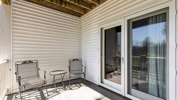 A covered porch with two metal chairs and a small table, a sliding glass door, and a wooden ceiling.