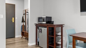 Una habitación compacta con kitchenette, una mesa de madera, una silla y un perchero.