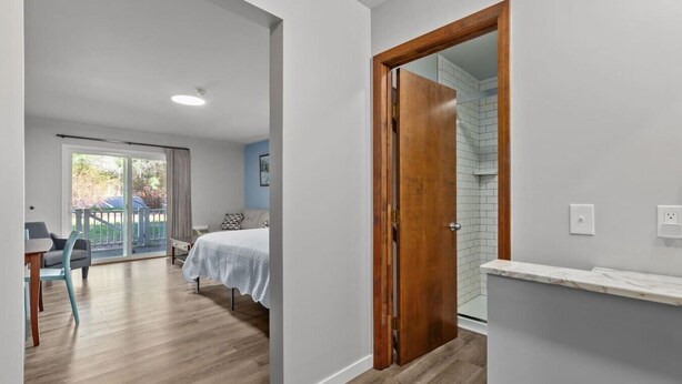 Un dormitorio con cama, un baño con ducha y un balcón con una silla.