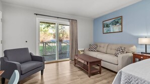 Habitación de hotel con sofá, sillón, mesa de centro de madera y un cuadro en la pared.