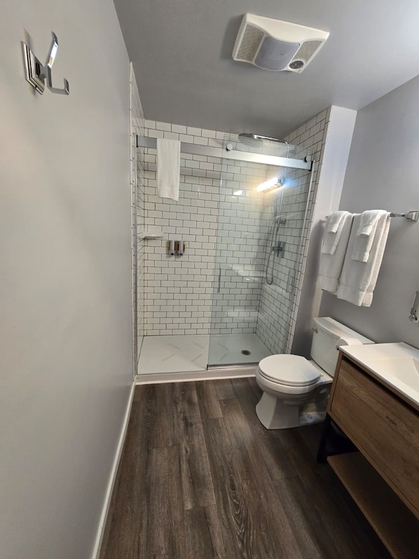 A modern bathroom with a glass shower enclosure, a white toilet, and a wooden vanity.