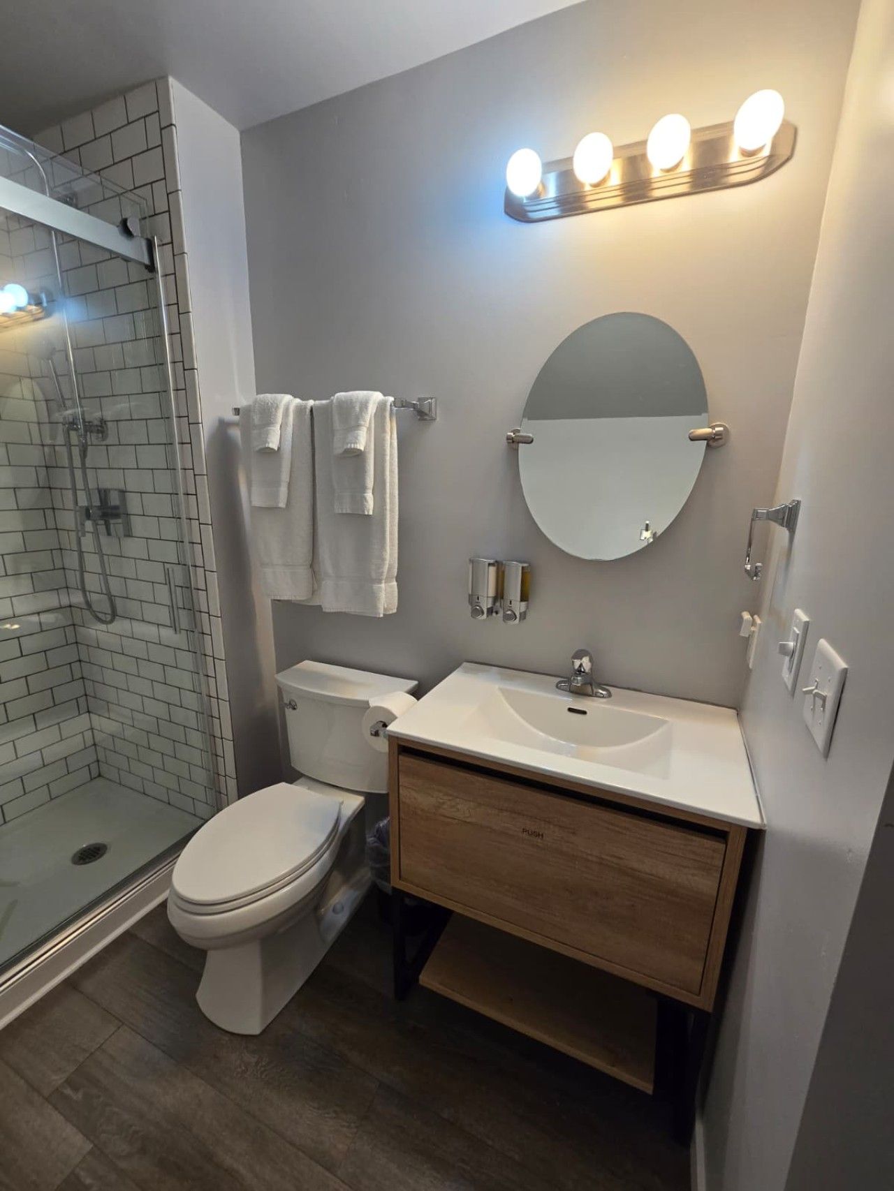 Une salle de bain moderne dotée d’une douche à parois de verre, de toilettes, d’un lavabo avec un miroir et d’un meuble-lavabo avec un placard en bois.