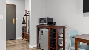 Une petite pièce comprenant un coin cuisine, une table en bois, une chaise et un porte-manteau.