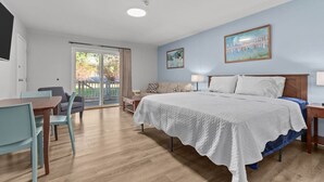 Une chambre d’hôtel comprenant un lit, un bureau, des chaises, un balcon avec vue et deux tableaux accrochés au mur.