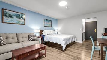 A room with a bed, a sofa, a wooden coffee table, and a desk with a chair.