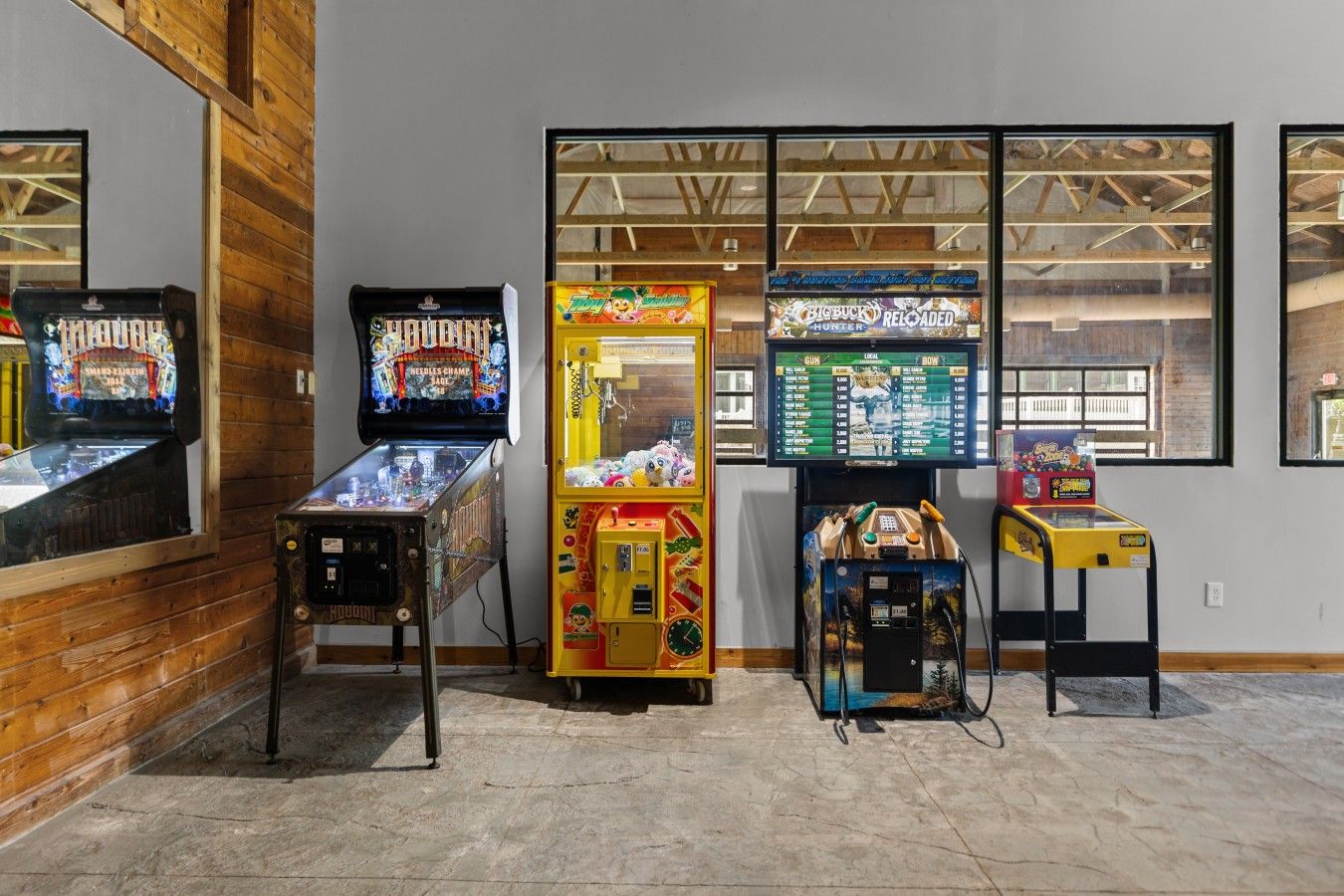 Une rangée de bornes d’arcade dans une pièce aux murs en bois, avec une fenêtre donnant sur l’extérieur.
